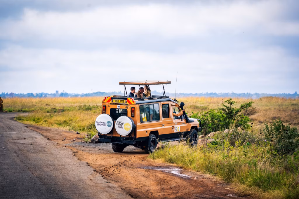En safari-jeep ved vejkanten i den afrikanske bush med passagerer, der kigger ud gennem bilens åbne tag.