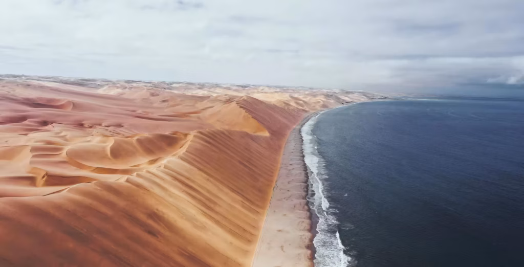 Sandwich Harbour i Namibia set fra oven med høje klitter, en strand og havet på den anden side.